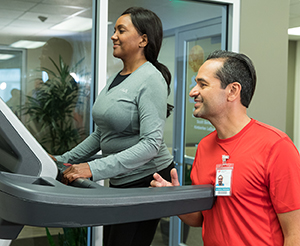 Woman on treadmill being coached by physical therapist.